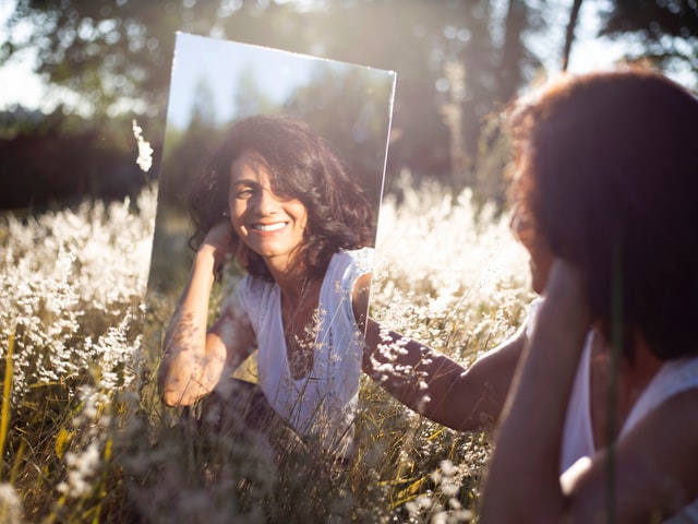 A girl sitting in a garden looking into the mirror 