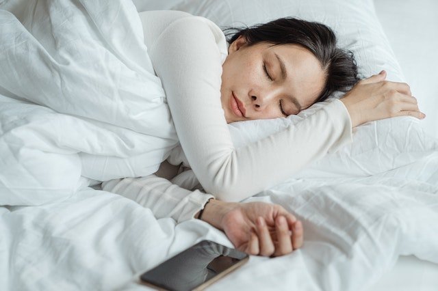 woman sleeping on a white bed with her mobile next to her