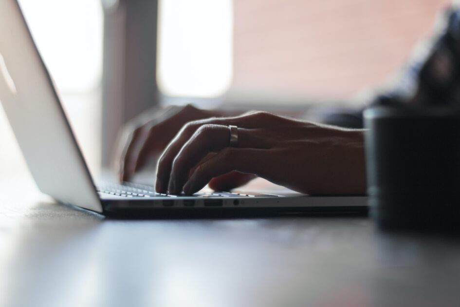 Someone working on a laptop with a cup right next to the laptop