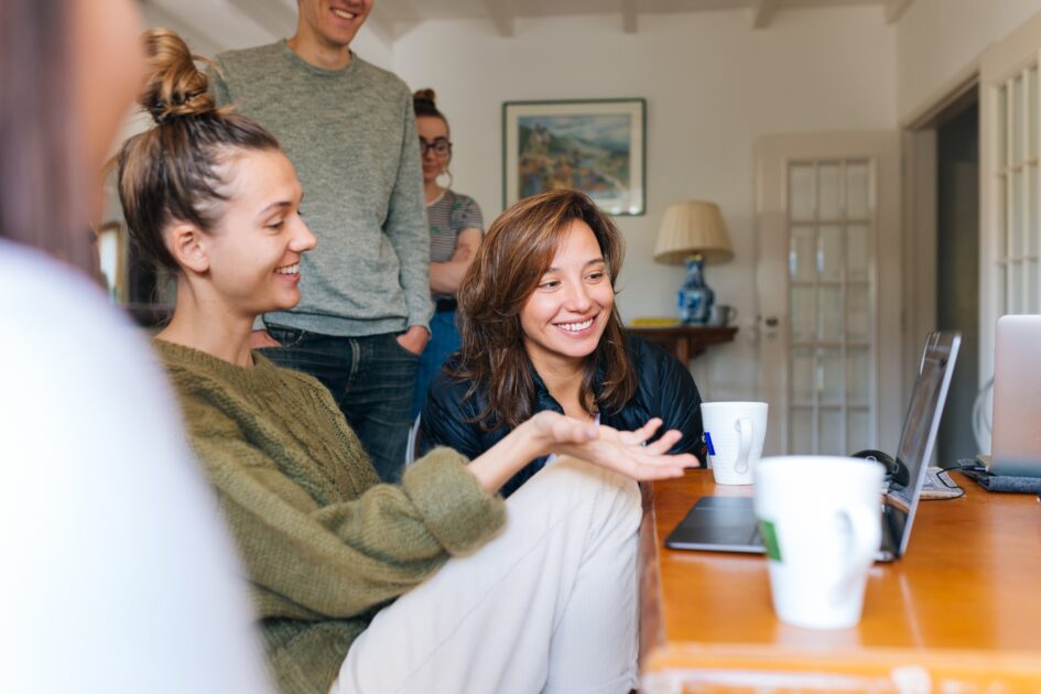 five people watching something on laptop and smiling