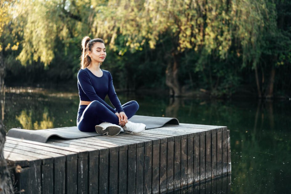 A girl sitting with her eyes closed near a pond