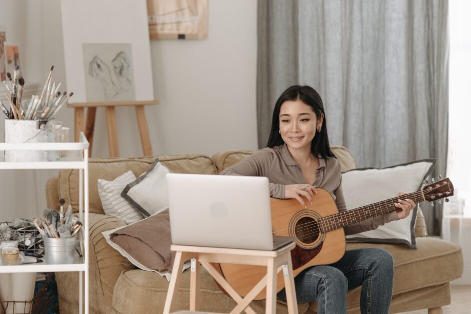 a girl is learning to play guitar from her laptop