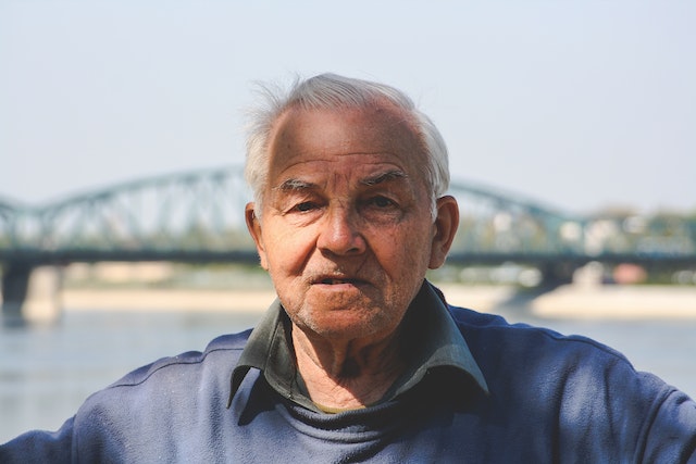 An old aged man looking in the camera near a bridge