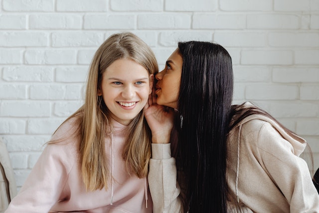 A teenage girl whispering in the other girl's ear